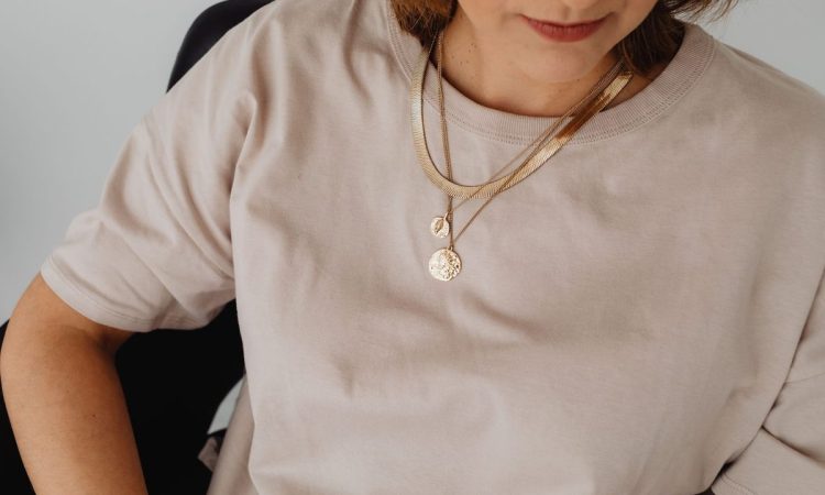 Une femme porte un t-shirt beige et un collier doré